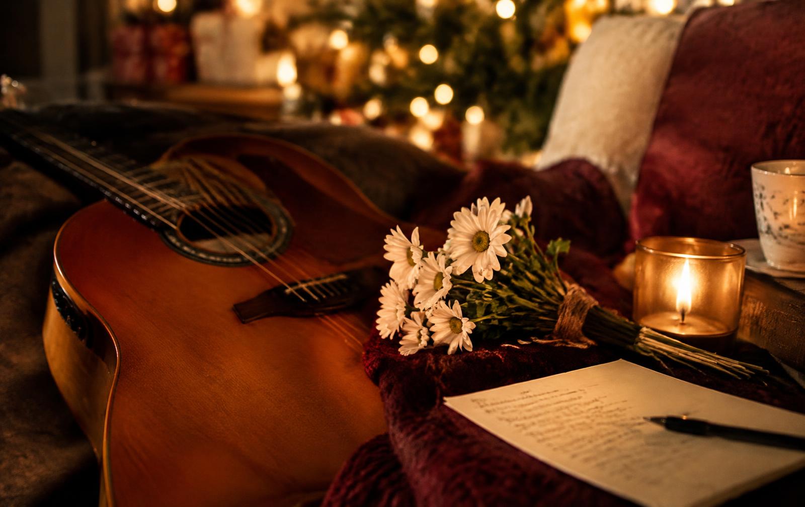 Guitar, daisies and handwritten lyrics by candlelight